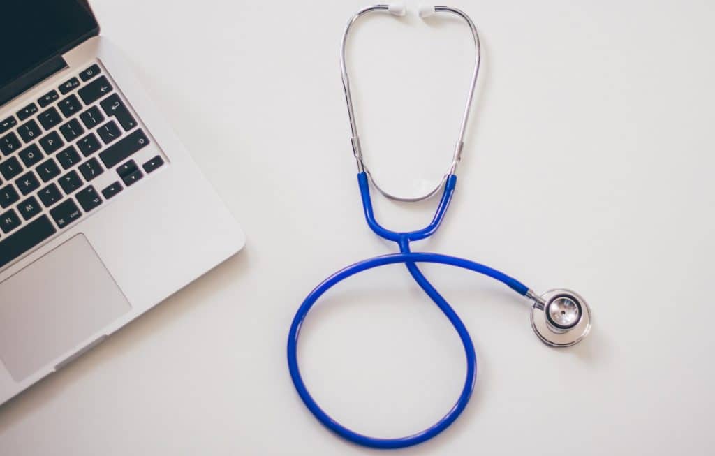 A silver laptop and a blue stethoscope lying on a desk