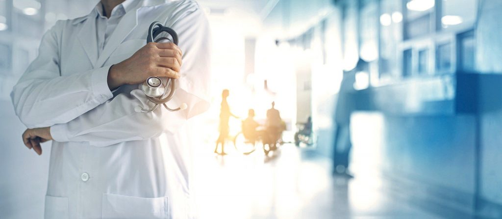 A physician with a stethoscope in his right hand wearing a white lab coat is standing in the ward of a hospital in Germany.