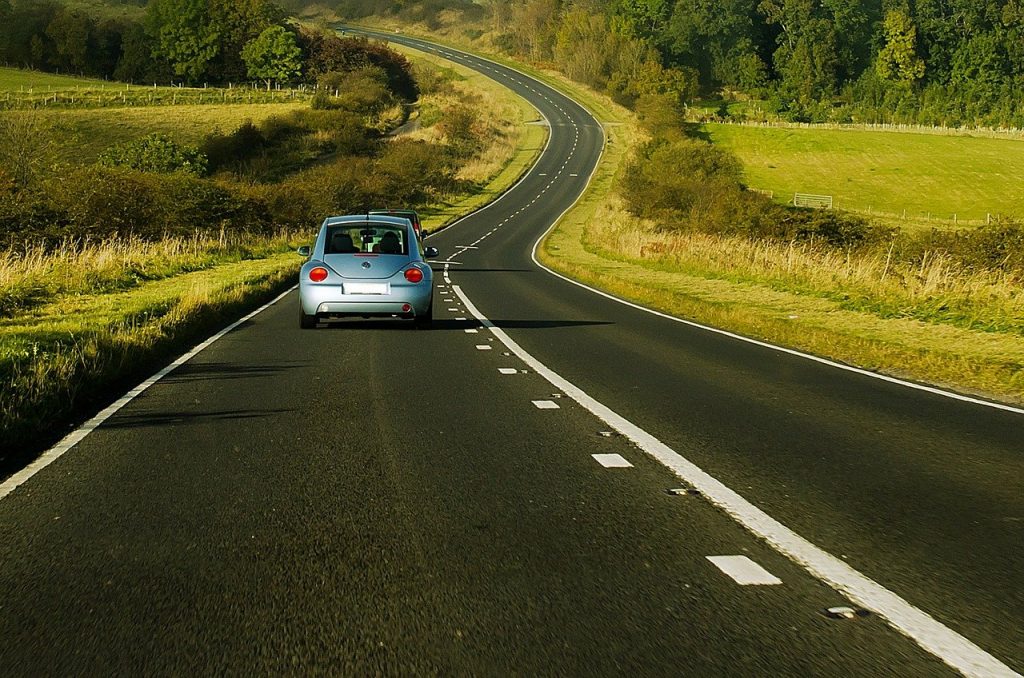 A car driving on an empty road surrounded by green nature